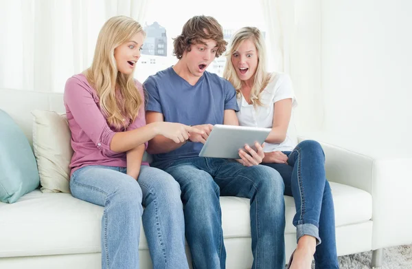 Drei Freunde blicken schockiert auf den Bildschirm des Tablets und — Stockfoto