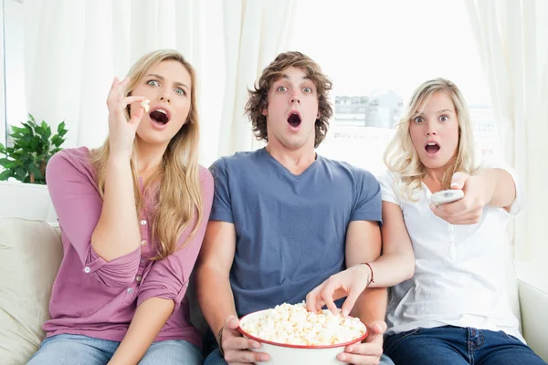 Tre vänner njuta av popcorn tillsammans medan chockade på tv — Stockfoto