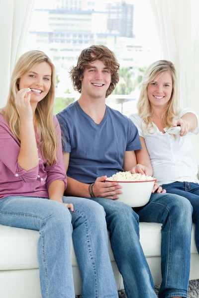 Tres amigos comiendo palomitas de maíz mientras sonríen y a punto de cambiar —  Fotos de Stock