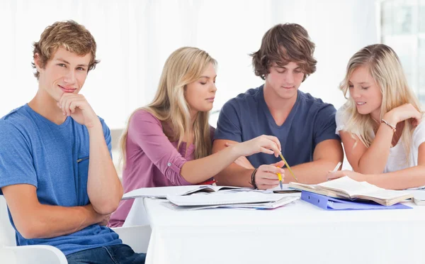 Four friends studying as one guy looks at the camera and smiles — Stock Photo, Image