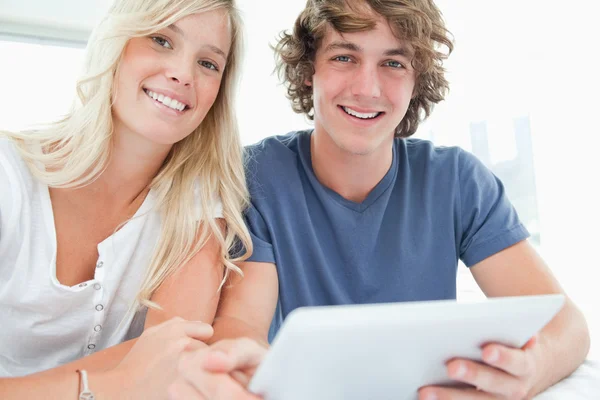 Ein lächelndes Paar hält ein Tablet in der Hand und blickt in die Kamera — Stockfoto