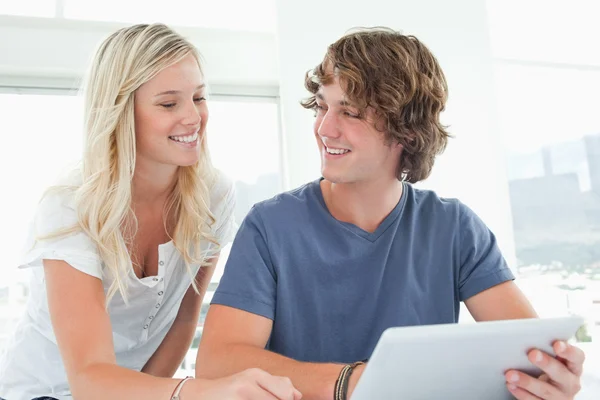Um casal sorrindo segurando um tablet e olhando um para o outro — Fotografia de Stock