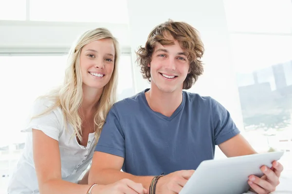 Ett leende par hålla en tablett och titta på kameran — Stockfoto