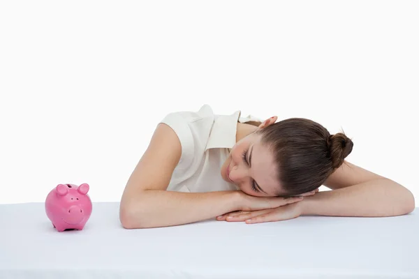 Businesswoman leaning on her desk looking at a piggy bank — Stock Photo, Image