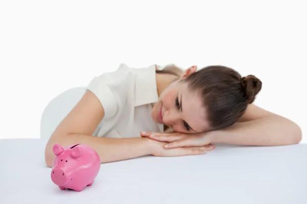 Jonge zakenvrouw leunend op haar bureau met een piggy bank — Stockfoto
