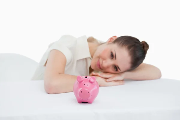Glimlachende zakenvrouw leunend op haar bureau met een piggy bank — Stockfoto