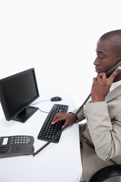 Side view of a secretary answering the phone while using a compu — Stock Photo, Image