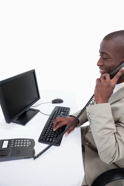Zijaanzicht van een mannelijke secretaris beantwoorden de telefoon tijdens het gebruik van een — Stockfoto