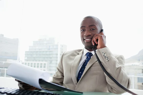 Улыбающийся бизнесмен по телефону во время чтения документа — стоковое фото