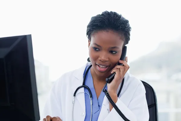 Vrouwelijke arts aan de telefoon tijdens het gebruik van een computer — Stockfoto