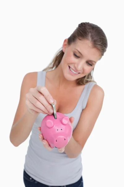 Portrait of a woman putting a note in a piggy bank — Stock Photo, Image