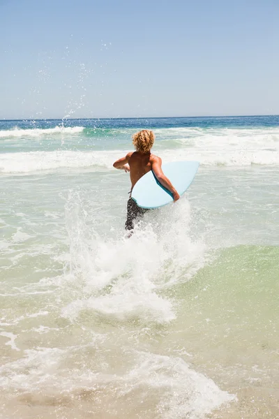 Blond człowiek działa szybko w wodzie, trzymając jego deskę surfingową Zdjęcie Stockowe