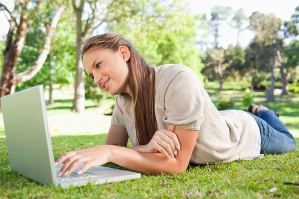 Frau liegt mit Laptop auf dem Rasen Stockbild