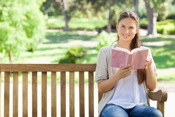 Woman sitting with a book on a park bench — Stock Photo, Image