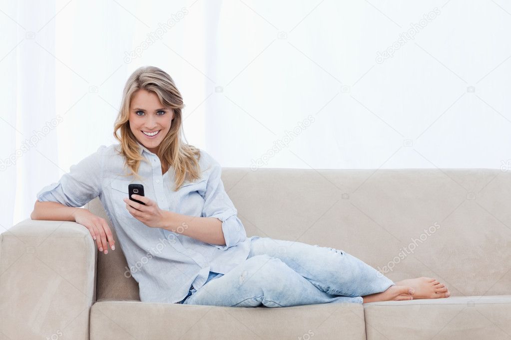 A woman sitting on a couch holding a mobile phone is smiling — Stock ...