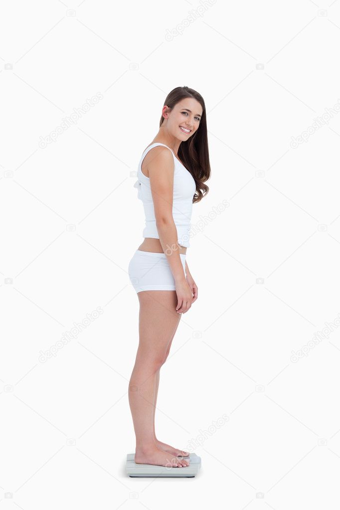 Download - Side view of a woman standing on weighing scales while looking a...