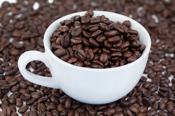 Pequeña taza de café blanco en ángulo con granos de café — Foto de Stock