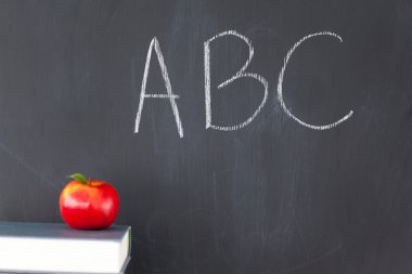 Stack of books with a red apple and a blackboard with 