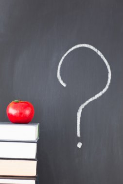 Stack of books with a red apple and a blackboard with 