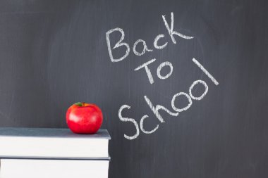 Stack of books with a red apple and a blackboard with 