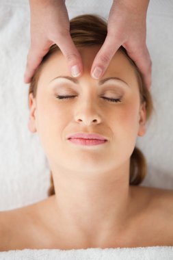 Cute blond-haired woman getting a massage on her face clipart