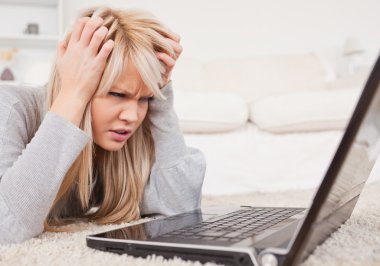 Attractive blond woman frustrated with her computer lying on a c clipart