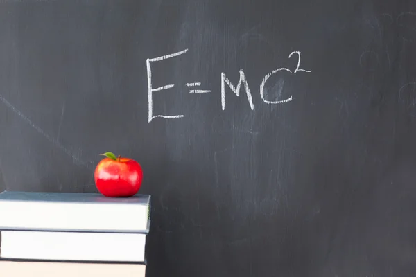 Stack of books with a red apple and a blackboard with a formula — Stock Photo, Image