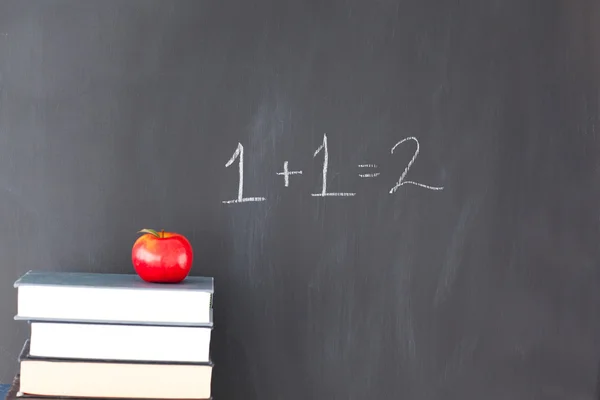 Stapel boeken met een rode apple en een schoolbord met oefening — Stockfoto