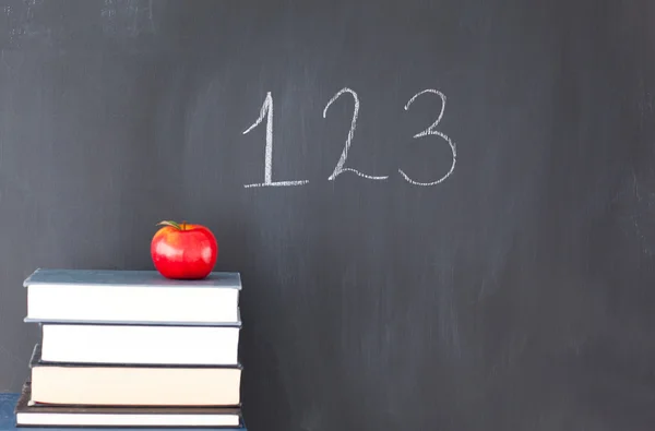 Pilha de livros com uma maçã vermelha e um quadro negro com "123" escrito — Fotografia de Stock