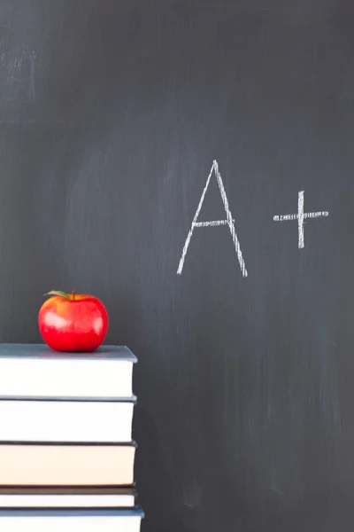Куча книг с красным яблоком и доска с буквой "А +". — стоковое фото