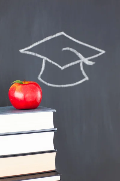 Bücherstapel mit einem roten Apfel und einer Tafel mit einem Absolventen — Stockfoto