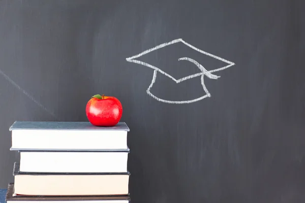 Bücherstapel mit einem roten Apfel und einer Tafel mit einem Absolventen — Stockfoto