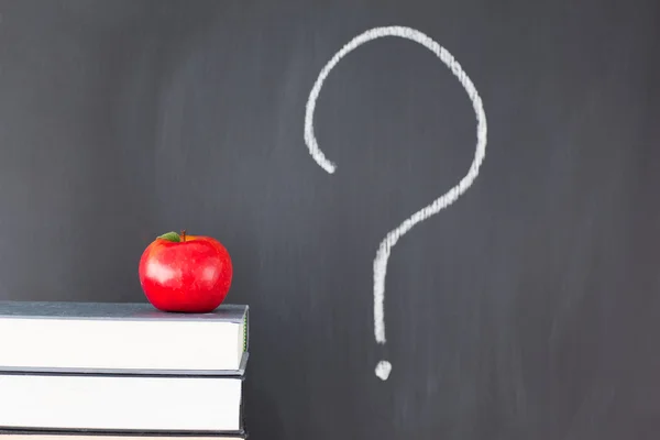 Stack of books with a red apple and a blackboard with "?" writte — Stock Photo, Image
