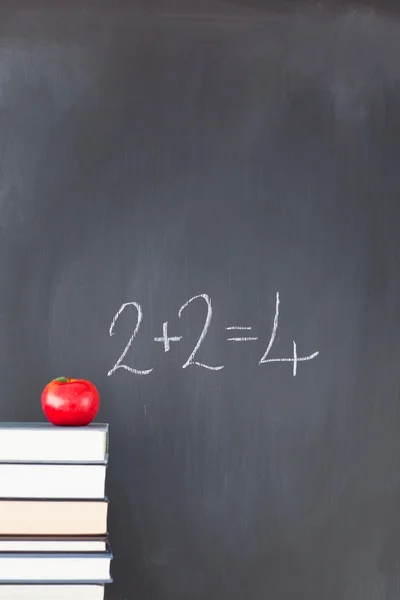 Stapel boeken met een rode apple en een schoolbord met oefening — Stockfoto