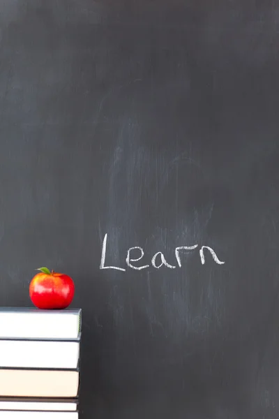Stack of books with a red apple and a blackboard with "learn" wr — Stock Photo, Image