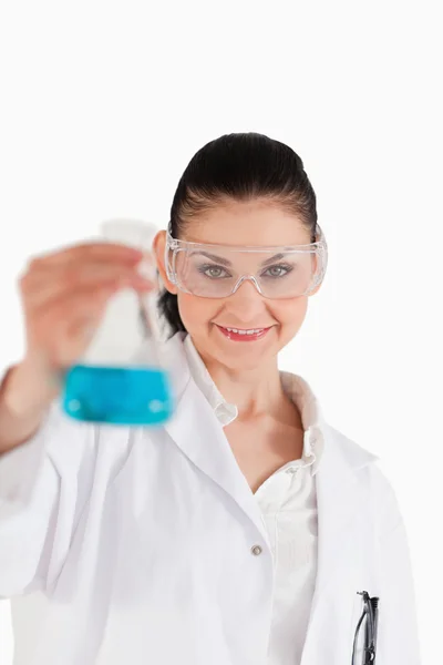 Cientista de cabelos escuros com óculos de segurança segurando um frasco azul — Fotografia de Stock