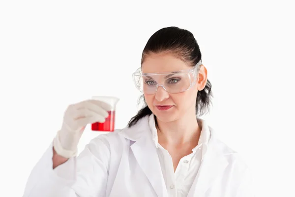 Científico de cabello oscuro mirando un vaso de precipitados rojo — Foto de Stock
