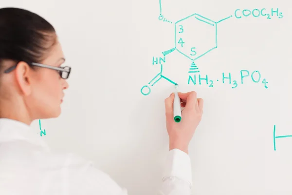 Mulher cientista de cabelos escuros escrevendo uma fórmula em um quadro branco — Fotografia de Stock