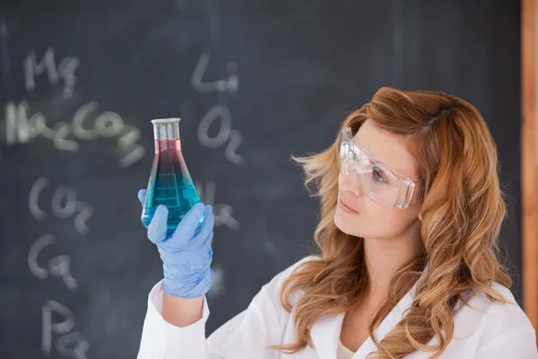 Jovem cientista olhando para um frasco vermelho e azul — Fotografia de Stock