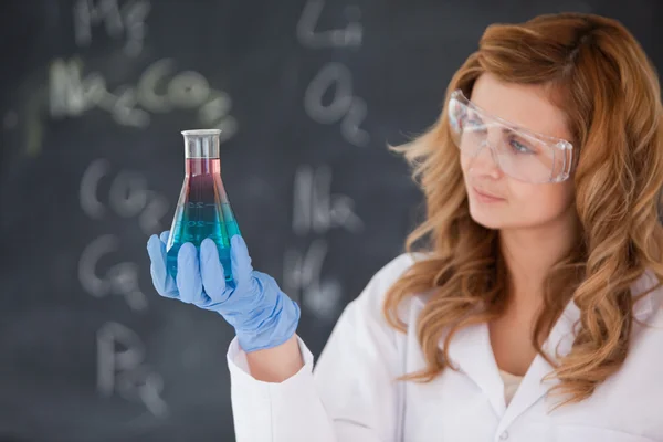 Young female scientist looking at a red and blue flask — Stock Photo, Image
