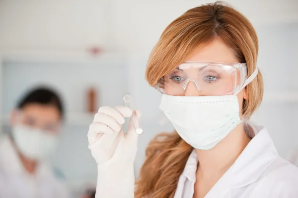 Blond-haired scientist wearing a mask and safety glasses and hol — Stock Photo, Image