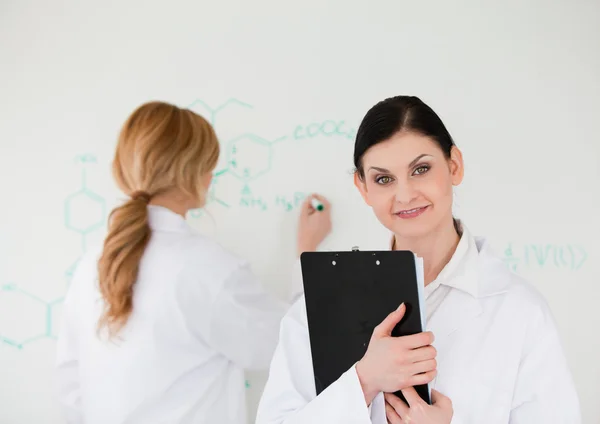Wissenschaftlerin schreibt mit Hilfe ihres Assistenten eine Formel — Stockfoto