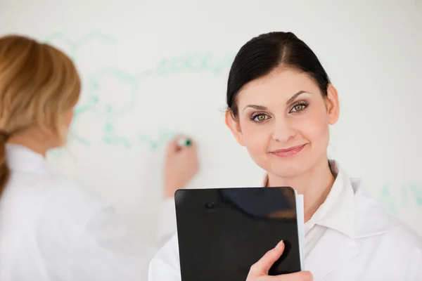 Cientista de cabelos loiros escrevendo uma fórmula ajudada por seu assistente — Fotografia de Stock