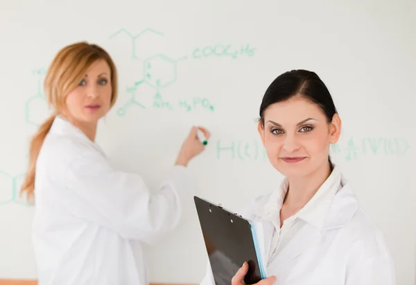 Cute scientist writting a formula helped by her assistant — Stock Photo, Image