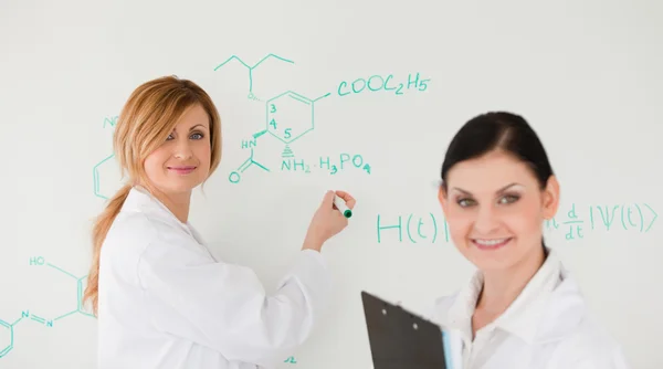 Científica atractiva escribiendo una fórmula ayudada por su asistente — Foto de Stock