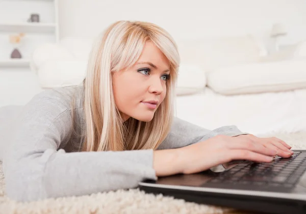 Schöne konzentrierte Frau entspannt auf einem Laptop liegend auf einem Carpe — Stockfoto