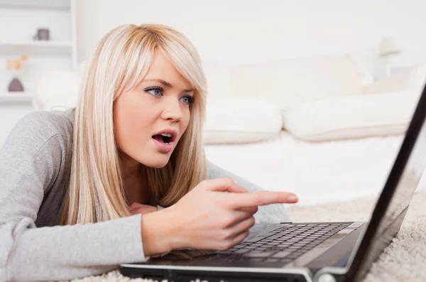Pretty blond woman frustrated with her computer lying on a carpe — Stock Photo, Image