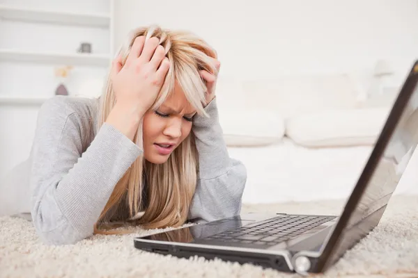 Attraente donna bionda arrabbiata con il suo computer sdraiato su un tappeto — Foto Stock