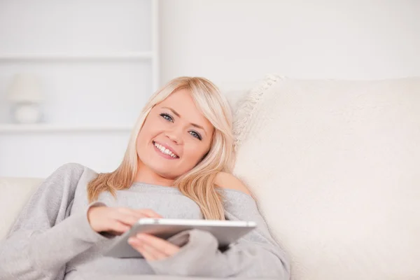 Hübsche blonde Frau liegt auf einem Sofa und entspannt sich auf einer Reihe von Tabletten — Stockfoto