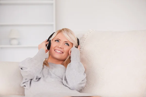 Attractive blond woman with headphones lying in a sofa — Stock Photo, Image
